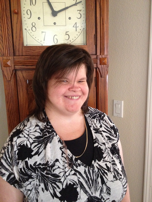 Elizabeth DeLong smiling, standing in front of a tall wooden clock.
